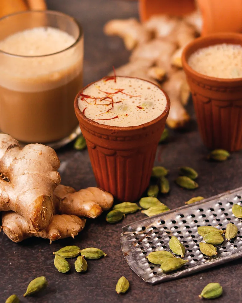 Chai in clay cups with fresh ginger root and cardamom pods
