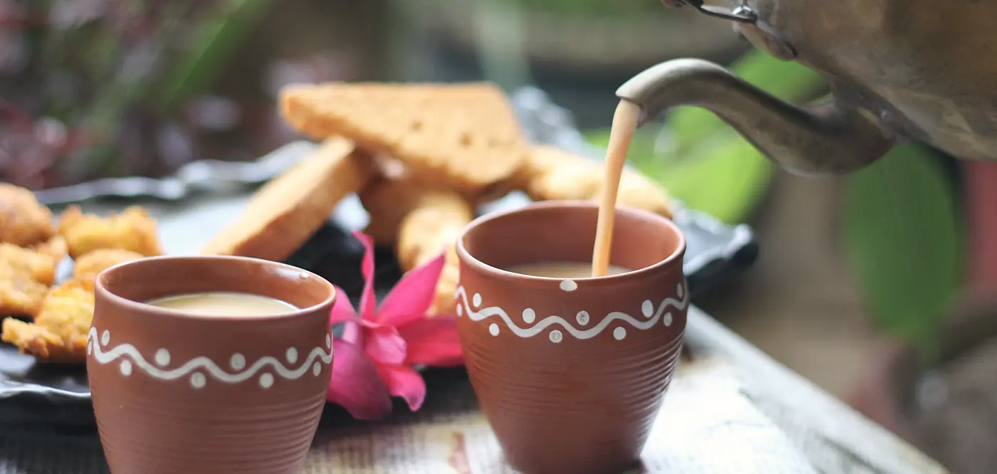 Chai poured from a brass kettle into clay cups