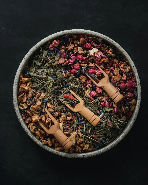A bowl of dried herbs, flowers and fruit with small wooden scoops