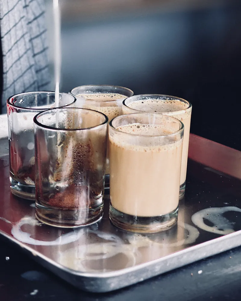 Milky chai strained into small glasses on a steel tray